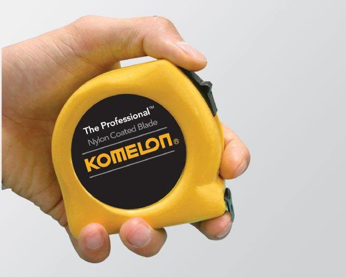 Hand holding a yellow Komelon 12-foot measuring tape with nylon coated blade in hand tools and measuring tools collections under $50