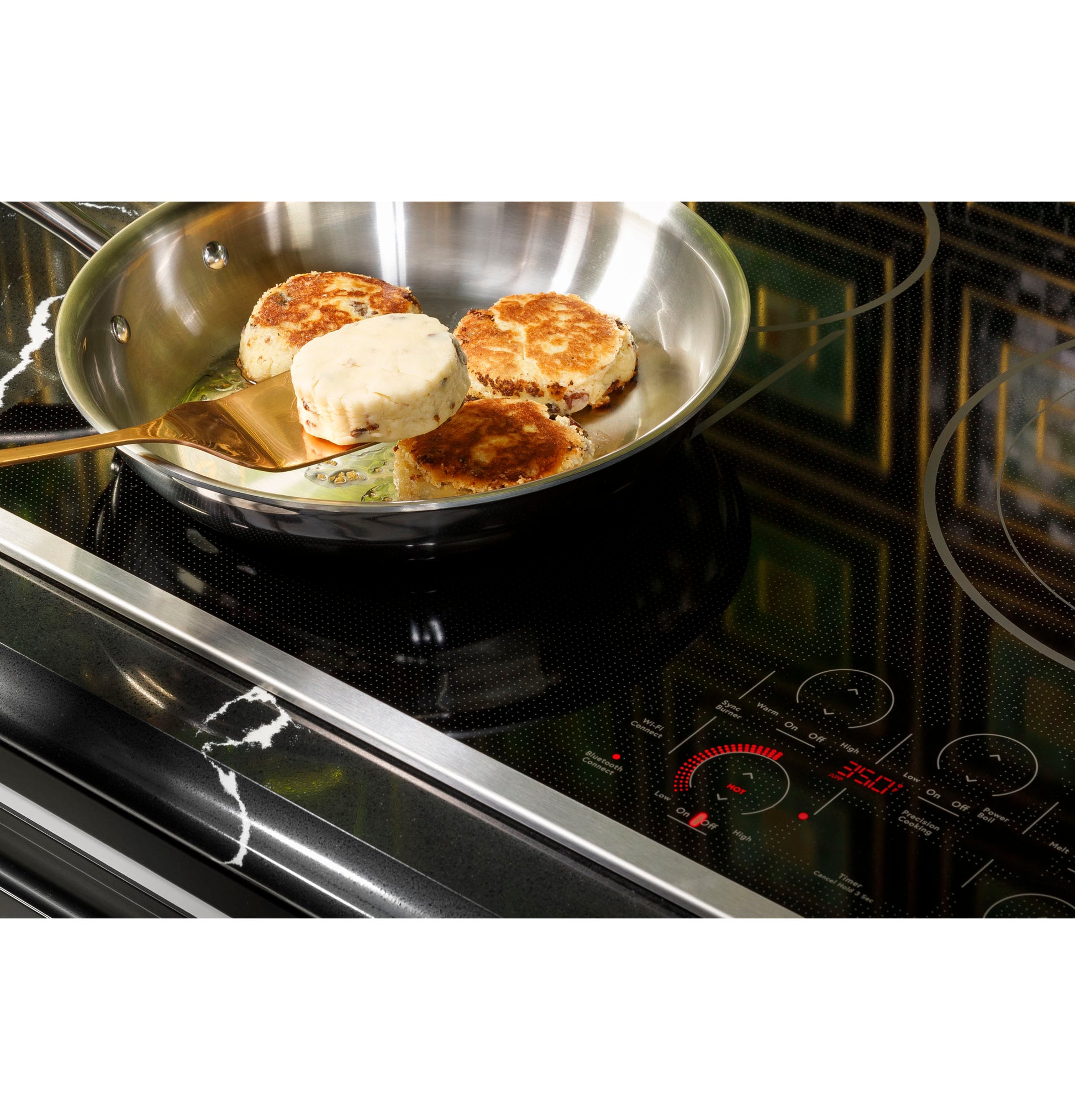 Close-up of a stainless steel pan cooking patties on a black touch-control electric cooktop with digital display and knobs