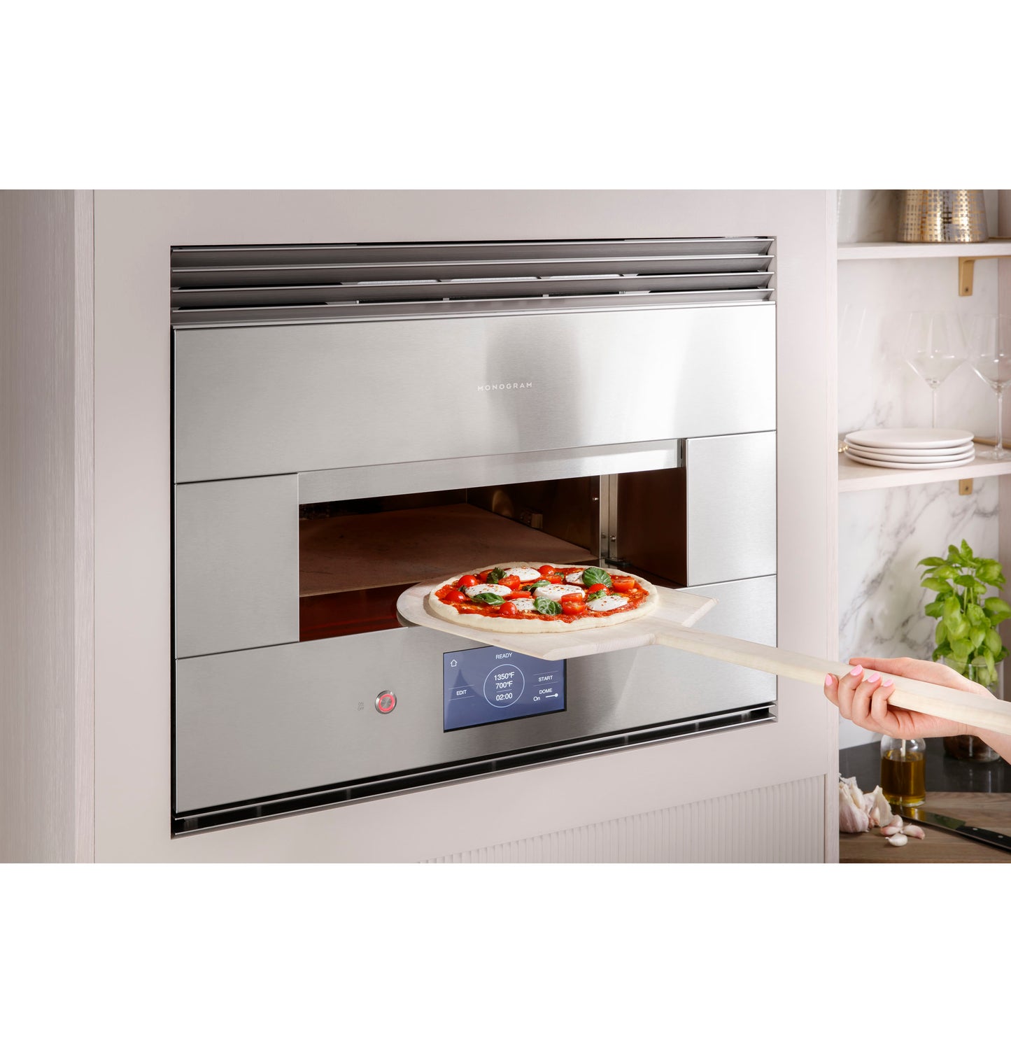 Stainless steel hearth oven with digital control baking a pizza in a modern kitchen with shelves and cookware