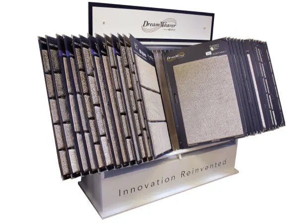 Rotating display rack showcasing multiple carpet sample boards in neutral shades, labeled with the DreamWeaver brand and the phrase Innovation Reinvented.