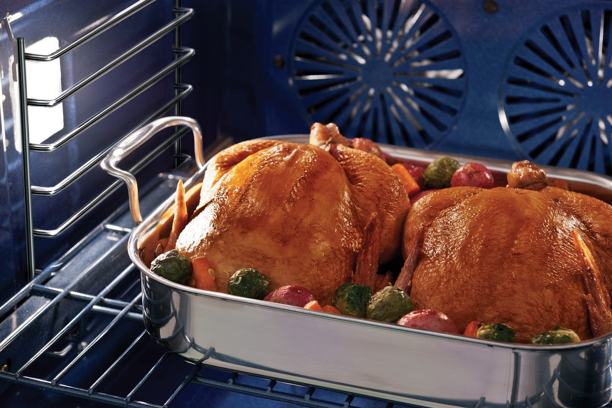 Two golden brown roasted chickens with vegetables cooking inside a blue interior double wall oven for home improvement