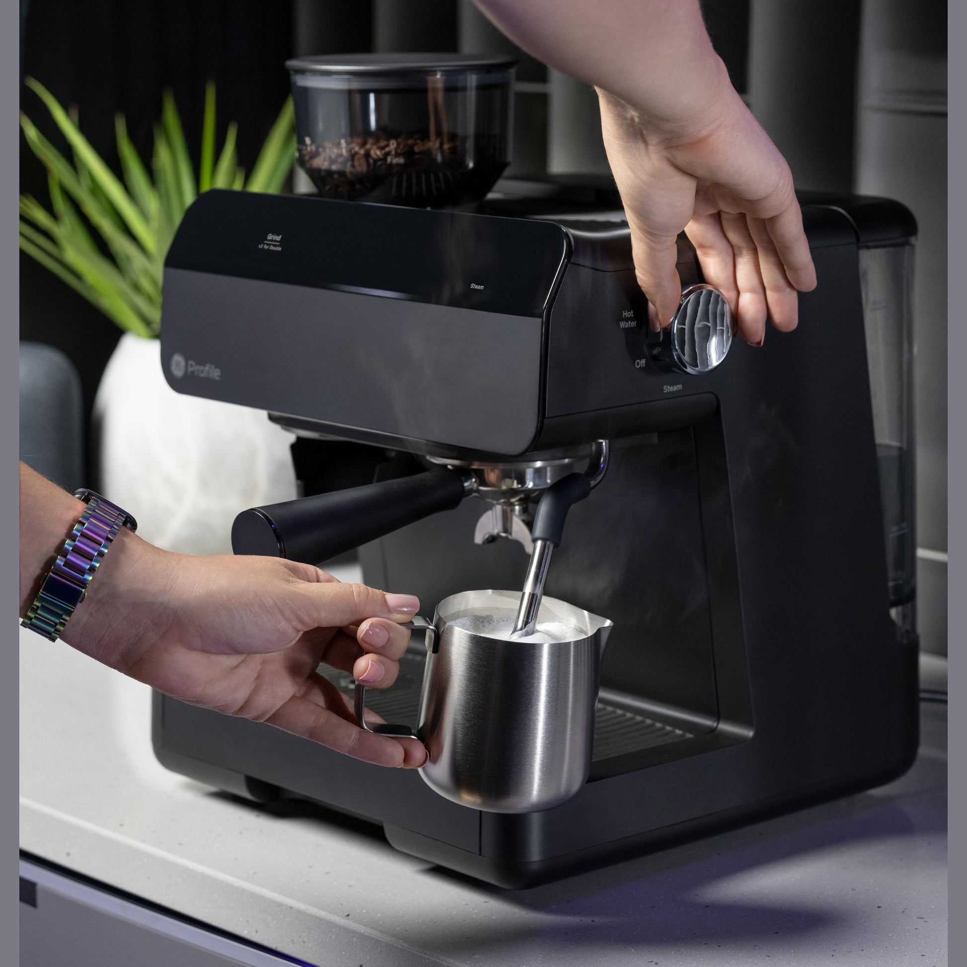 Black semi-automatic espresso machine with frother steaming milk in stainless steel pitcher on kitchen countertop