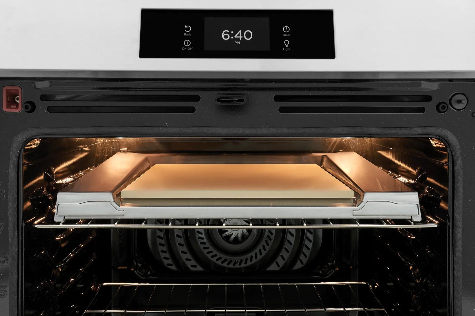 Interior view of a front control induction range oven with illuminated heating element and stone-baked pizza tray in home appliances