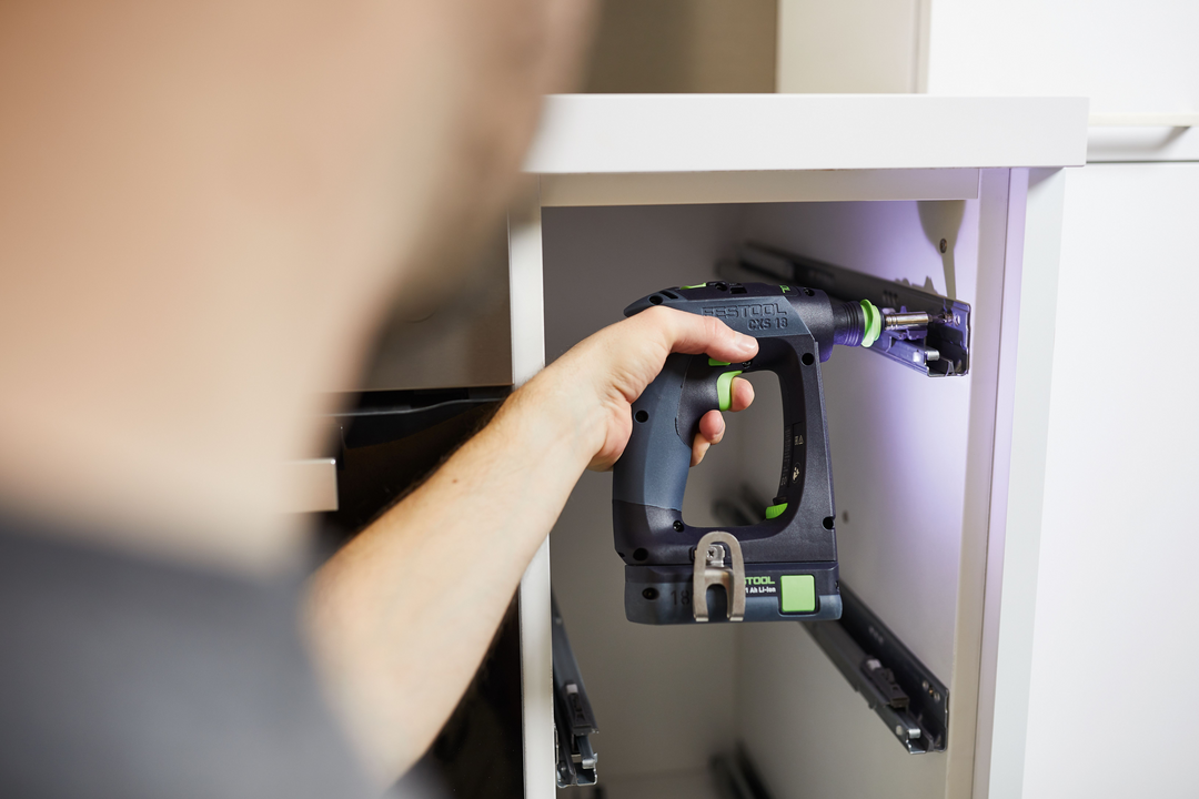 Person using compact Festool cordless drill to install drawer slides inside white cabinet during home improvement task