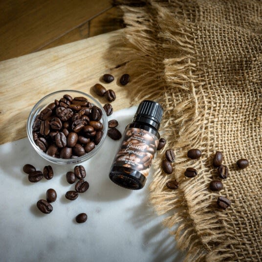 Small dark glass bottle of roasted espresso fragrance oil surrounded by coffee beans, burlap, and wood surface decor