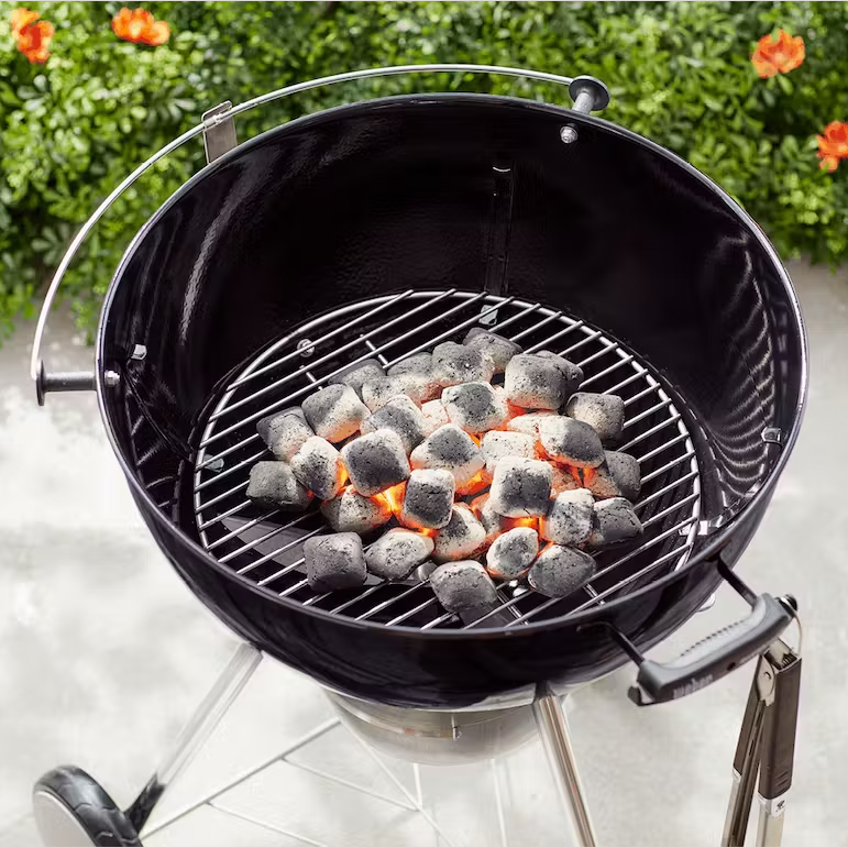 Round black kettle charcoal grill with steel grate and glowing briquettes for outdoor grilling and lawn use