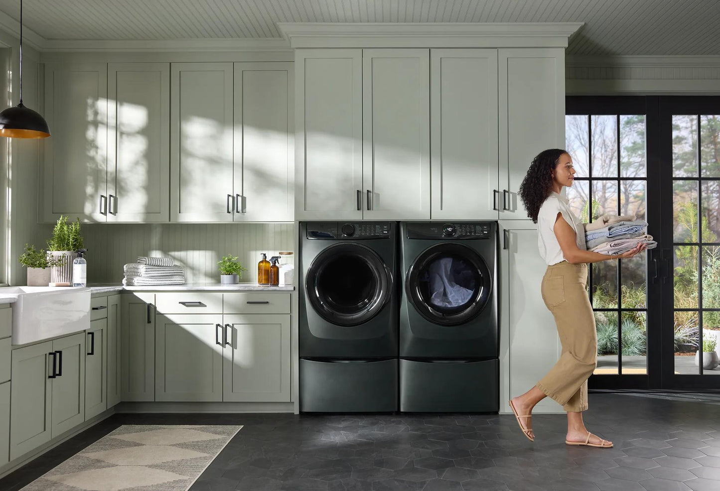 Dark gray front load electric washer and dryer pair in bright laundry room with white cabinetry and large glass door in appliances collection