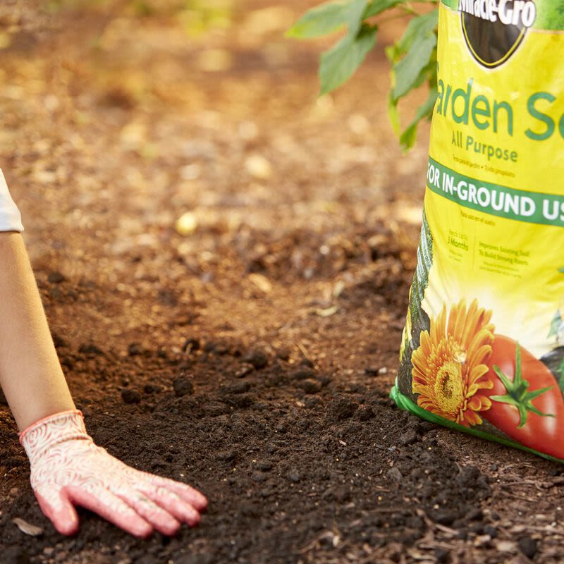 Person wearing patterned gardening gloves preparing soil next to a bag of all-purpose garden soil for outdoor living
