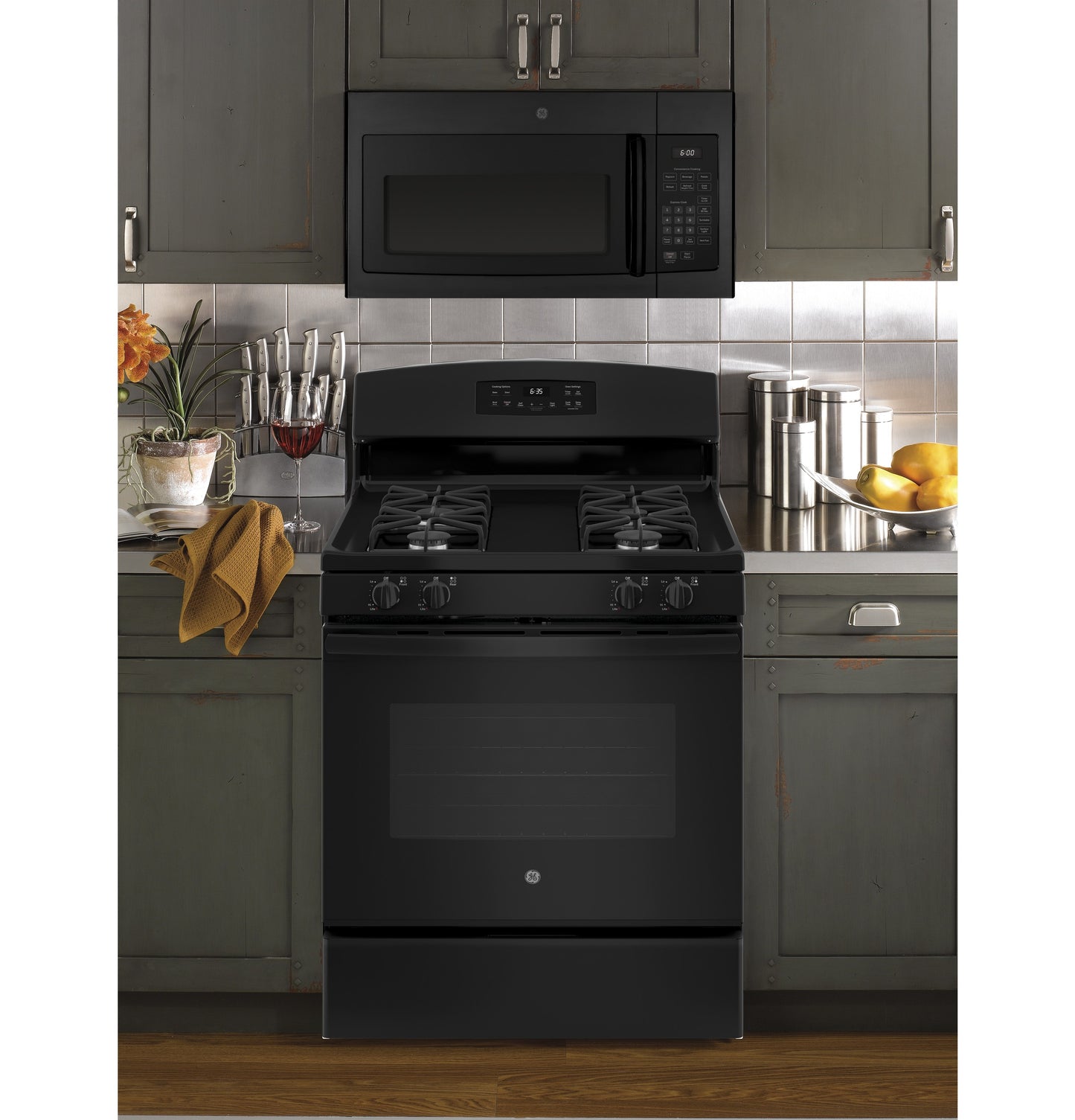 Black over-the-range microwave above black gas stove with four burners in kitchen with gray cabinetry and tiled backsplash
