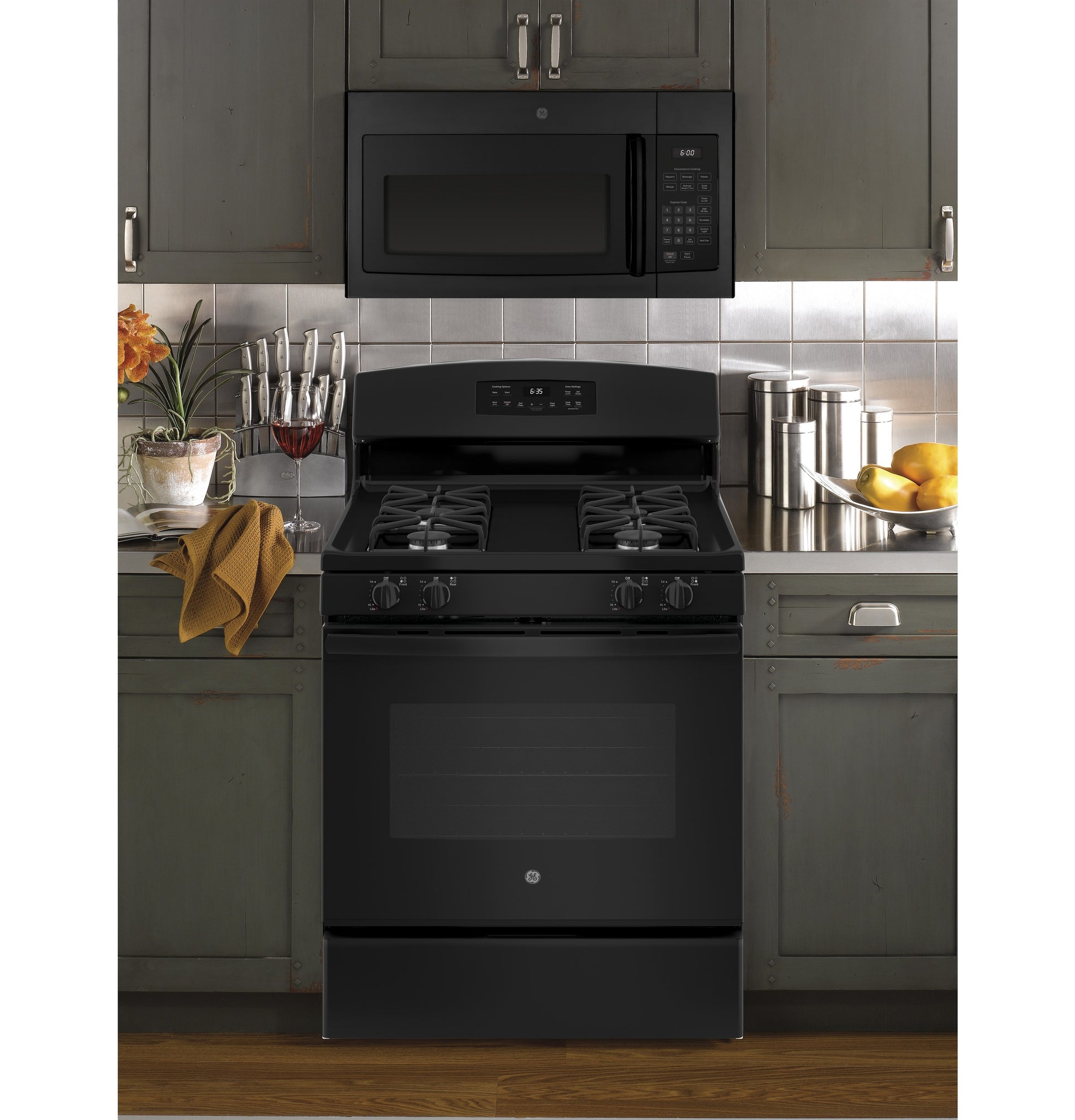 Black over-the-range microwave above black gas stove with four burners in kitchen with gray cabinetry and tiled backsplash