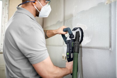 Worker smoothing drywall surface using Festool diamond grinder with dust extraction for home improvement project