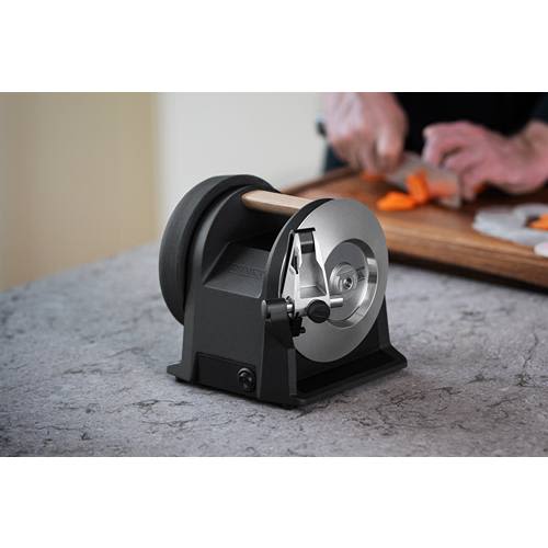 Black carbon kitchen knife sharpener with rotating grinding wheel and wooden handle on gray countertop for home use