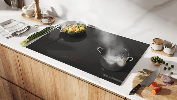 Modern black 30-inch induction cooktop without frame with two pots cooking vegetables and boiling water on wood kitchen counter
