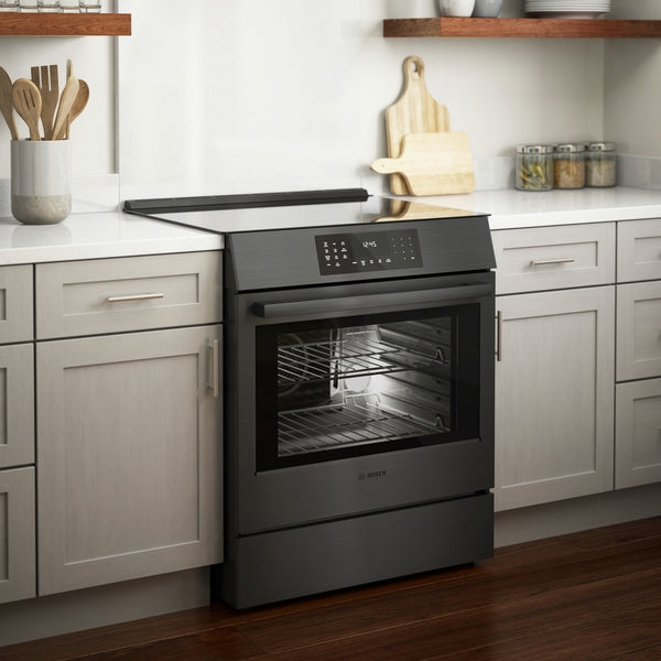Black stainless steel 30-inch induction slide-in range with digital controls and lighted oven interior in kitchen setting