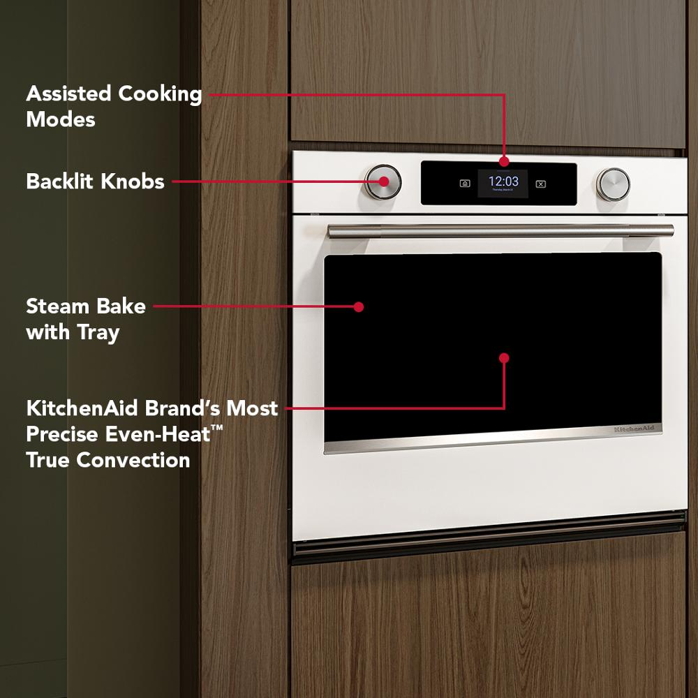 White smart electric wall oven with backlit knobs and assisted cooking modes built into modern wood cabinetry