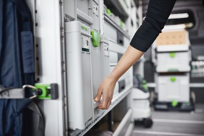 Hand reaching to pull a gray and green interlocking Festool tool storage systainer from truck storage system for workshop organization