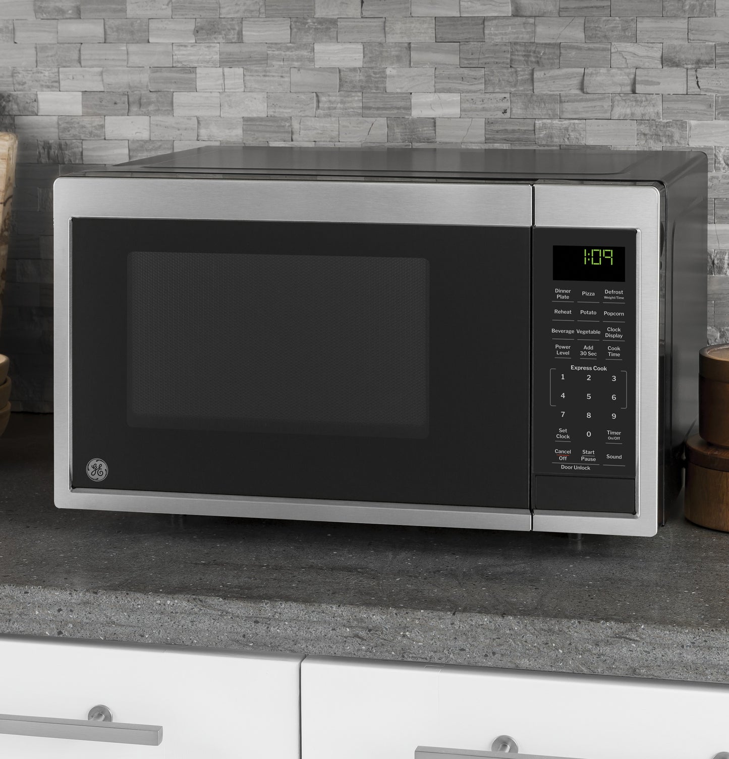 Stainless steel microwave oven with digital control panel on gray kitchen countertop, tile backsplash in appliance setting