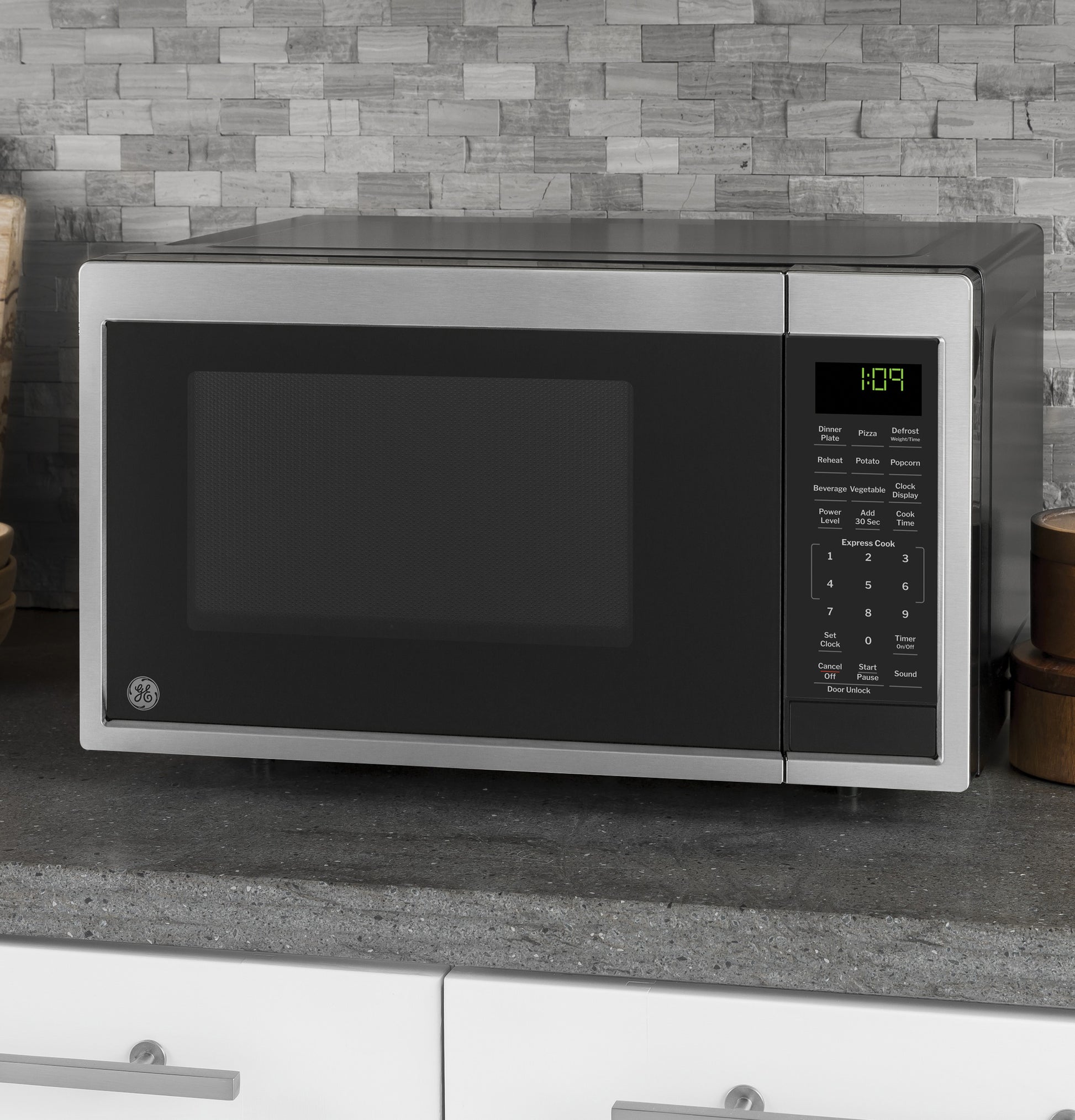 Stainless steel microwave oven with digital control panel on gray kitchen countertop, tile backsplash in appliance setting