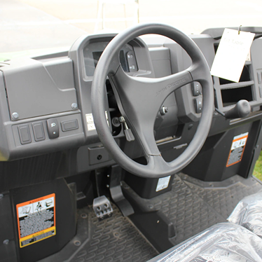 Steering wheel and control panel inside a John Deere utility vehicle with textured rubber floor mats visible