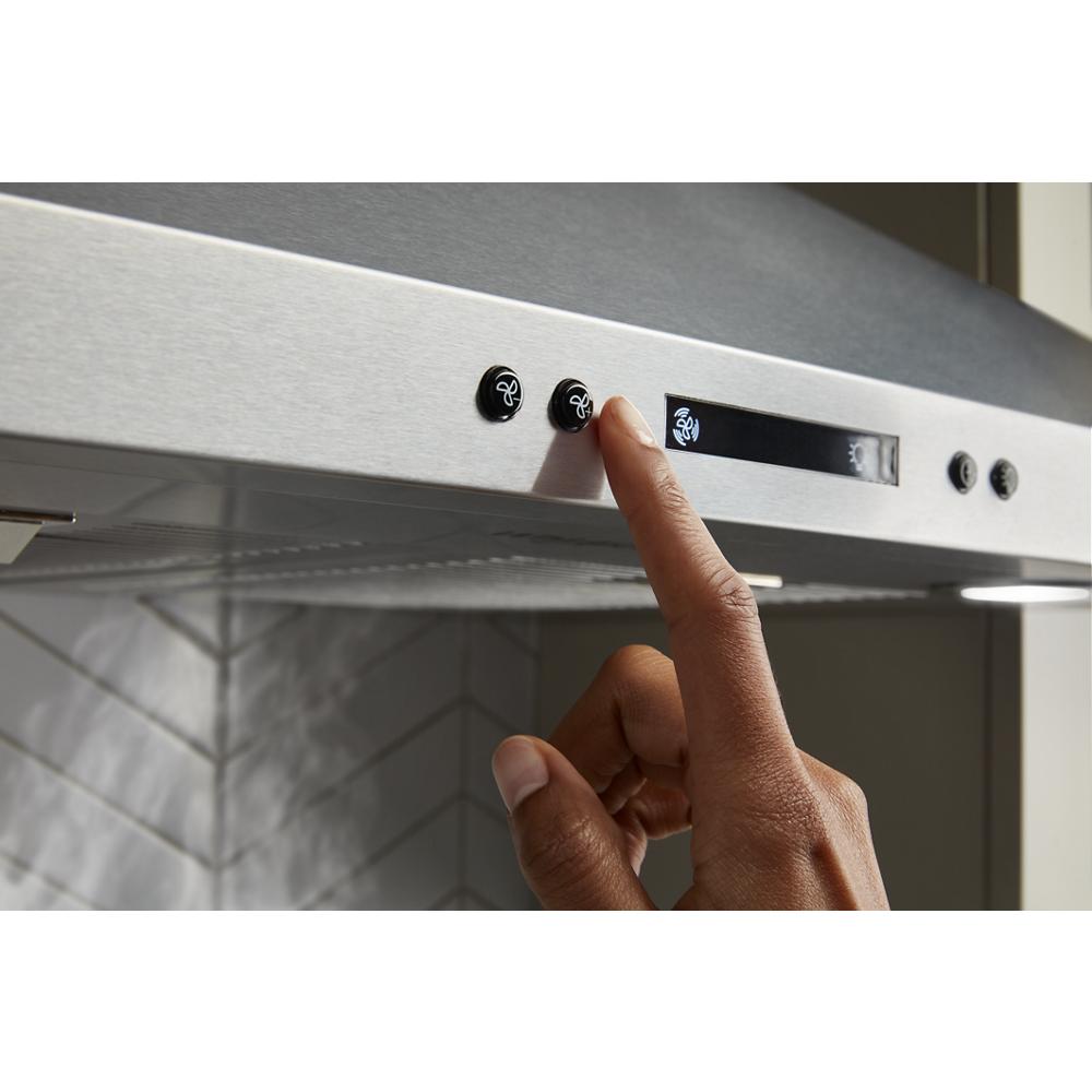 Finger pressing a button on a stainless steel chimney range hood control panel in kitchen appliances collection