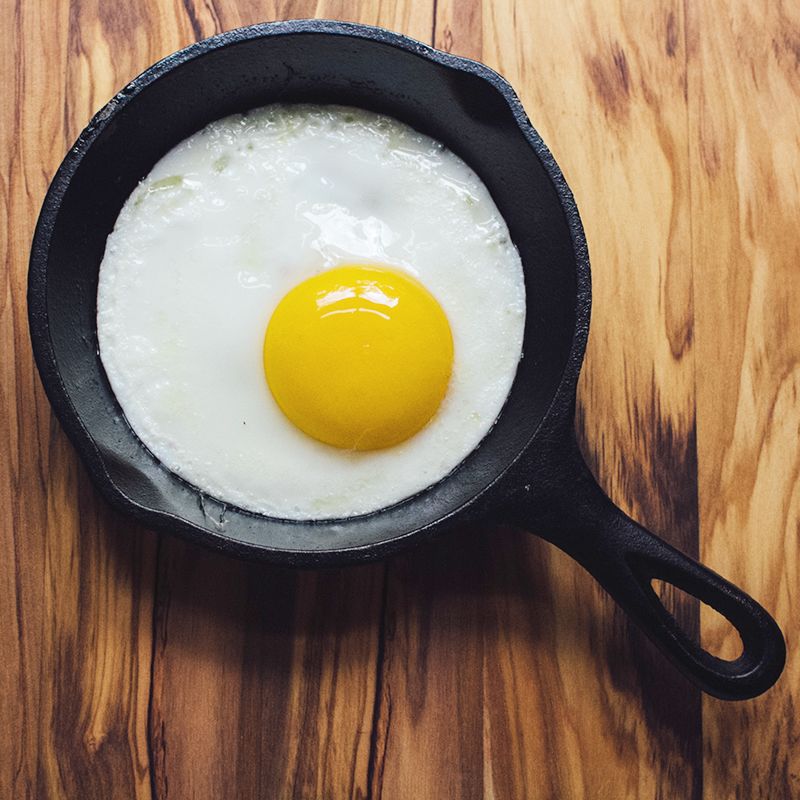 Black 5-inch heat treated mini cast iron skillet with cooked sunny-side-up egg on wood surface for home use