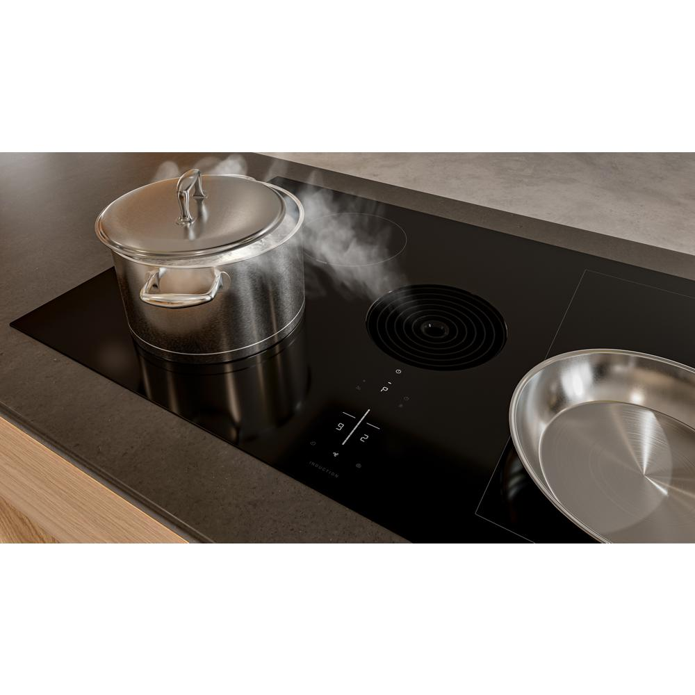 Black induction cooktop with steaming pot on heating zone and stainless steel pan beside on kitchen island counter