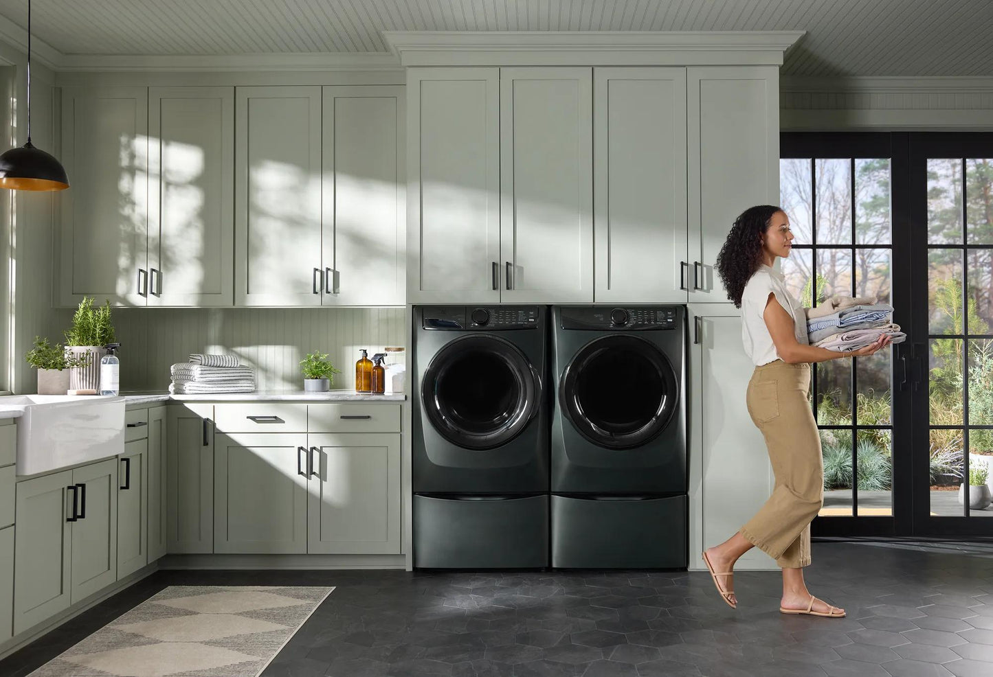 Modern laundry room with dark gray front load electric washer and dryer surrounded by white cabinetry and natural light