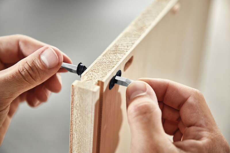 Hands inserting black center panel connectors into a light wood panel in woodworking tool accessories for home improvement projects