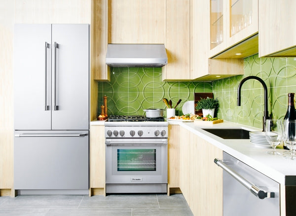 Modern kitchen with stainless steel appliances including refrigerator, range, custom insert hood, and dishwasher