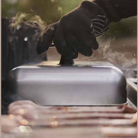 Hand with grilling glove lifting stainless steel basting dome over outdoor grill in outdoor living setup