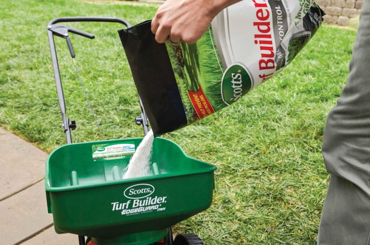 Pouring Scotts Turf Builder fertilizer into green spreader on lawn for lawn care and garden use