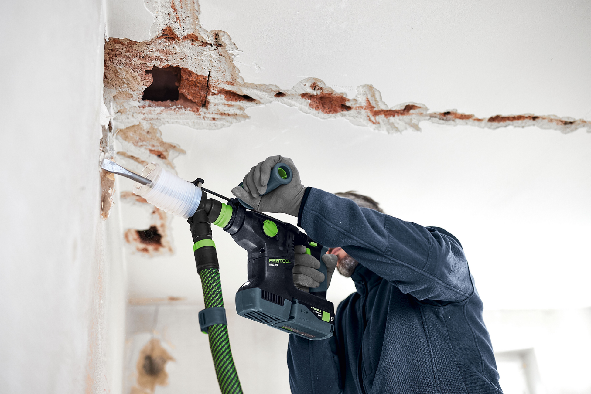 Worker using Festool cordless drill with dust extraction attachment on damaged wall in home improvement project