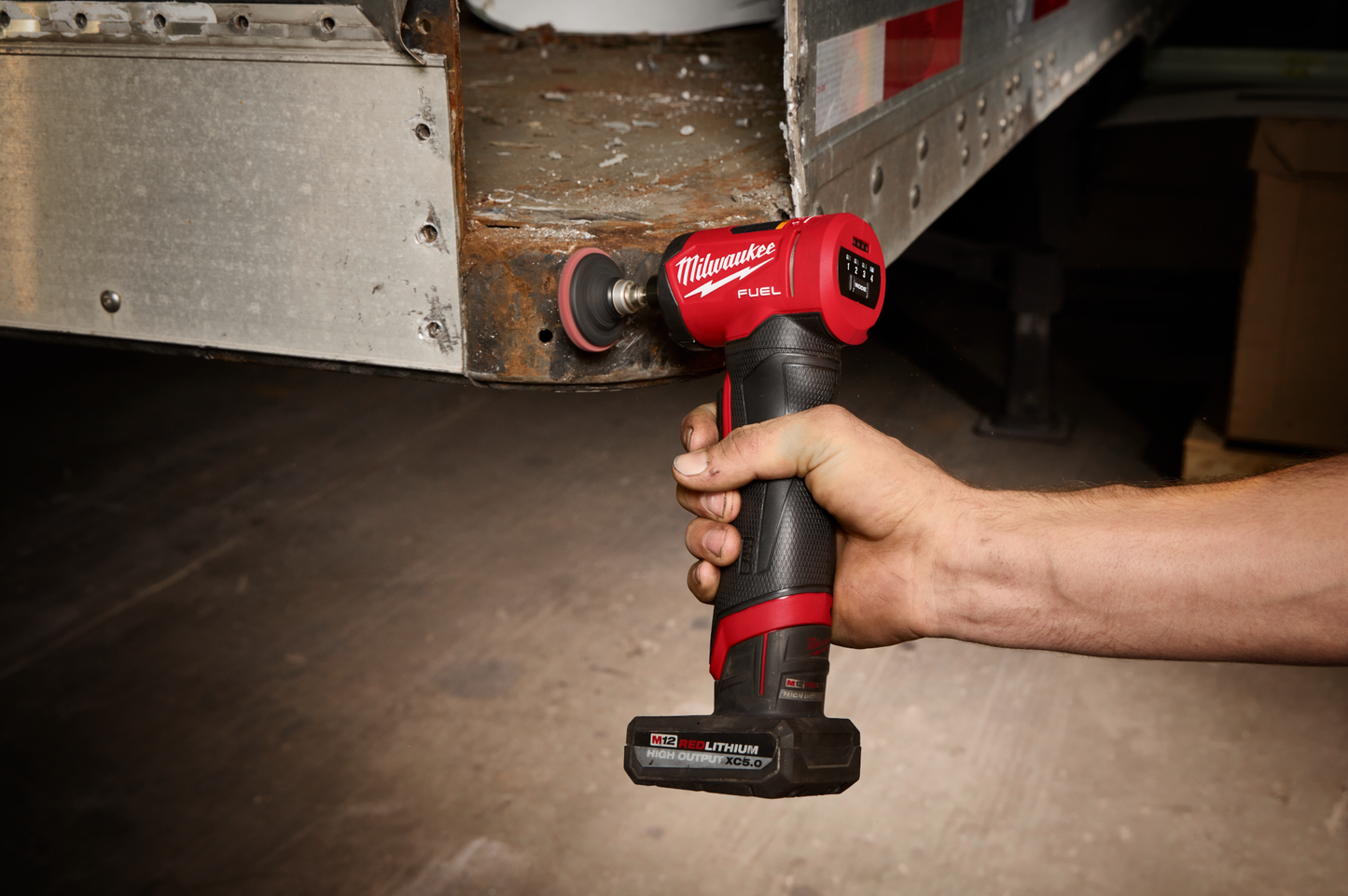 Handheld red and black cordless right angle die grinder polishing rusted metal edge in a workshop environment