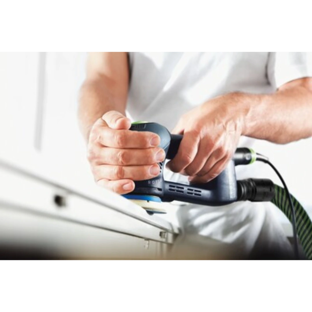 Person holding a Festool power sander with attached sanding pad smoothing a wooden surface in a workshop setting