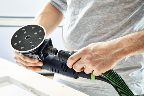 Person holding a cordless eccentric sander with dust extraction hose preparing for home improvement tasks