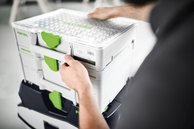Person unlocking a white Festool modular storage organizer with green latches in a workshop setting