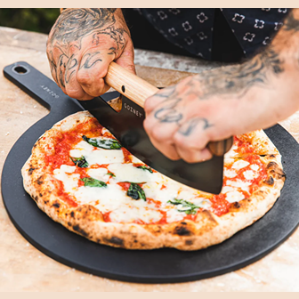 Black fiberboard pizza server with wooden handle used for slicing a freshly baked Margherita pizza outdoors