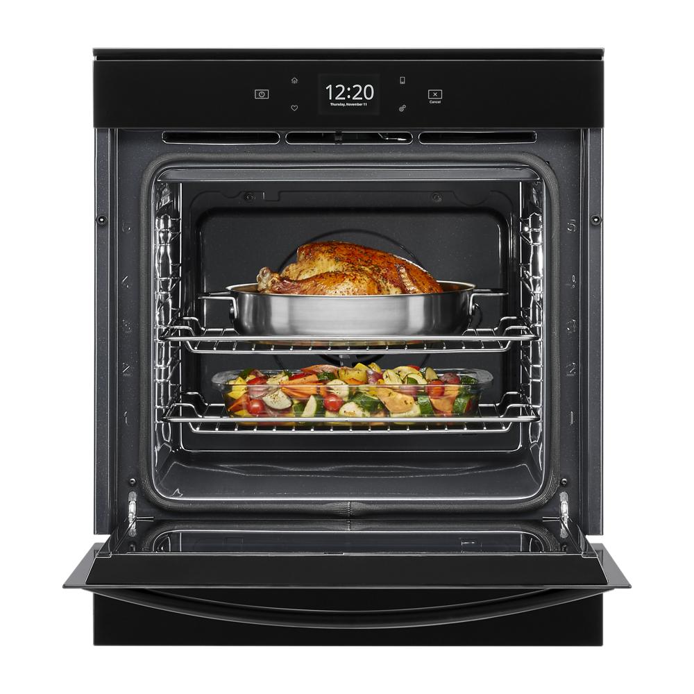 Open modern convection wall oven with cooked chicken and roasted vegetables on racks in kitchen appliances collection