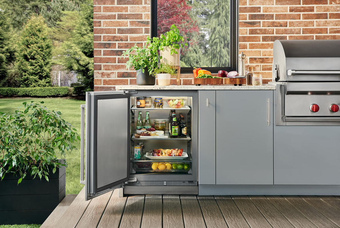 Outdoor under counter refrigerator with open door showing beverages and fresh produce inside kitchen and appliances collection