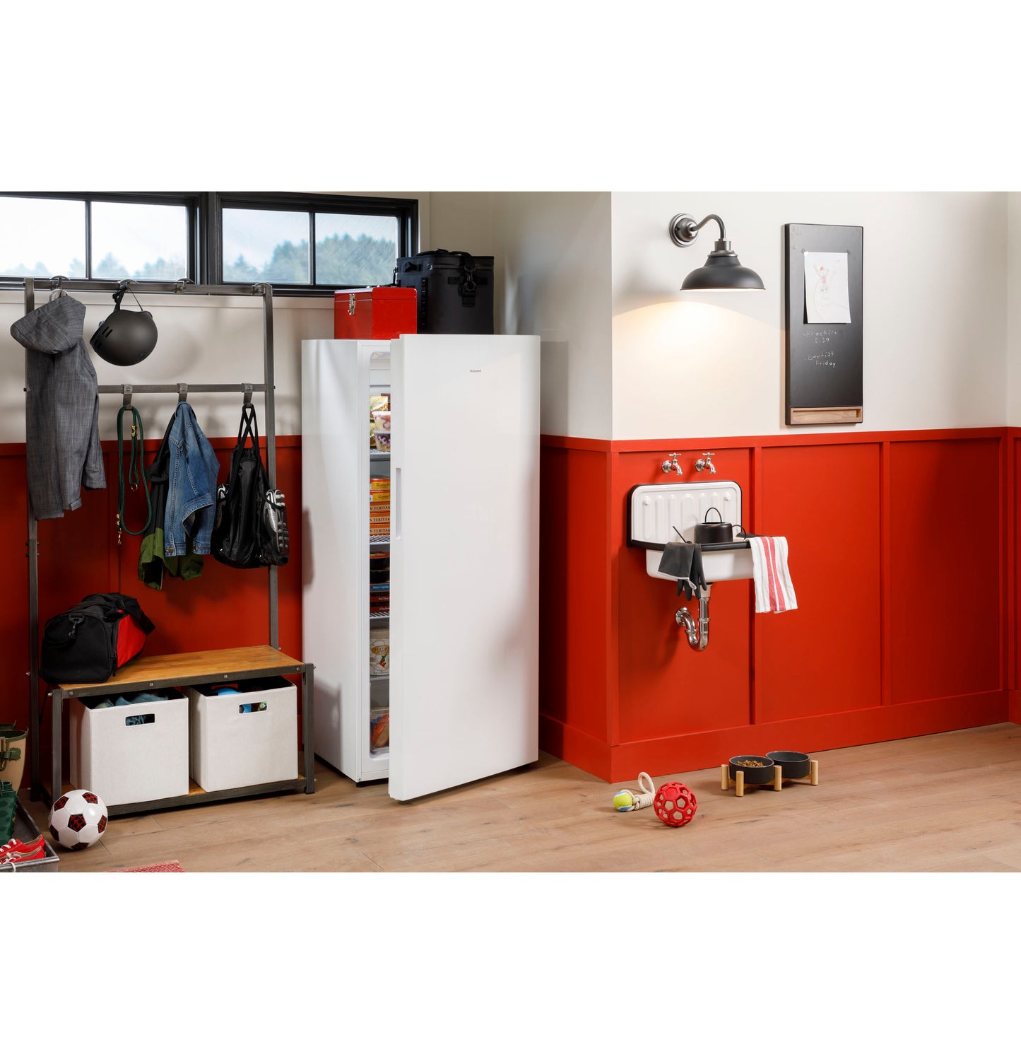 White upright freezer with open door in organized home entryway featuring red wainscoting and wooden floorboards