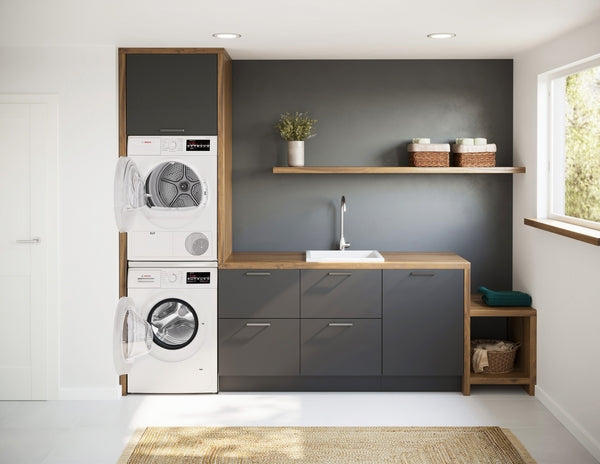 Stacked white front load compact washer and dryer integrated in modern gray cabinetry with wood accents and laundry sink