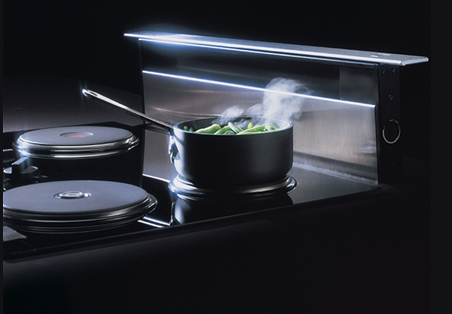 Modern broan downdraft ventilation system retracting behind stovetop with pot cooking green vegetables steaming