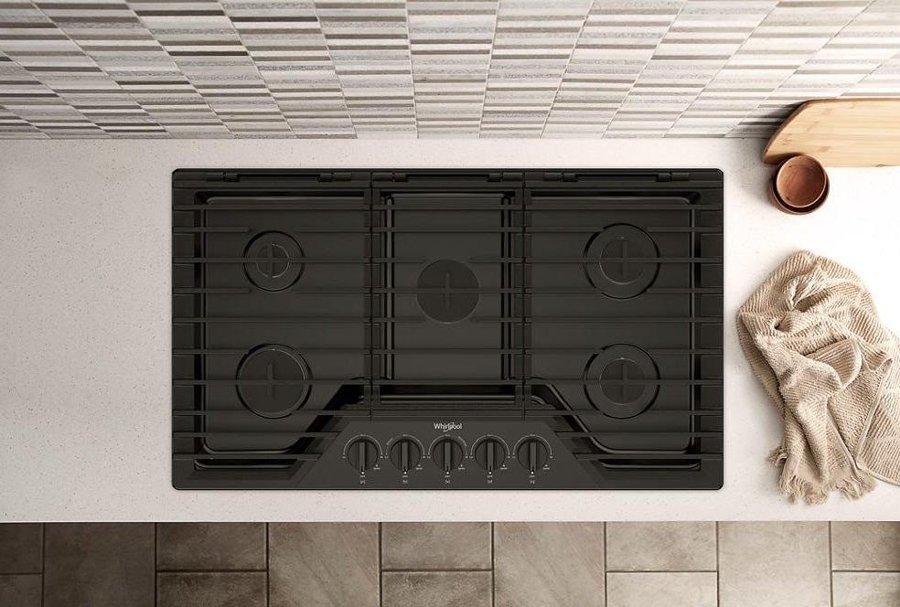 Black five-burner gas cooktop with hinged cast-iron grates installed in modern kitchen countertop setting