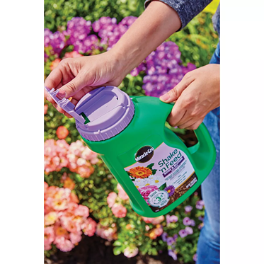 Green plant food container with purple lid being used in vibrant flower garden for plant care and lawn & garden collections