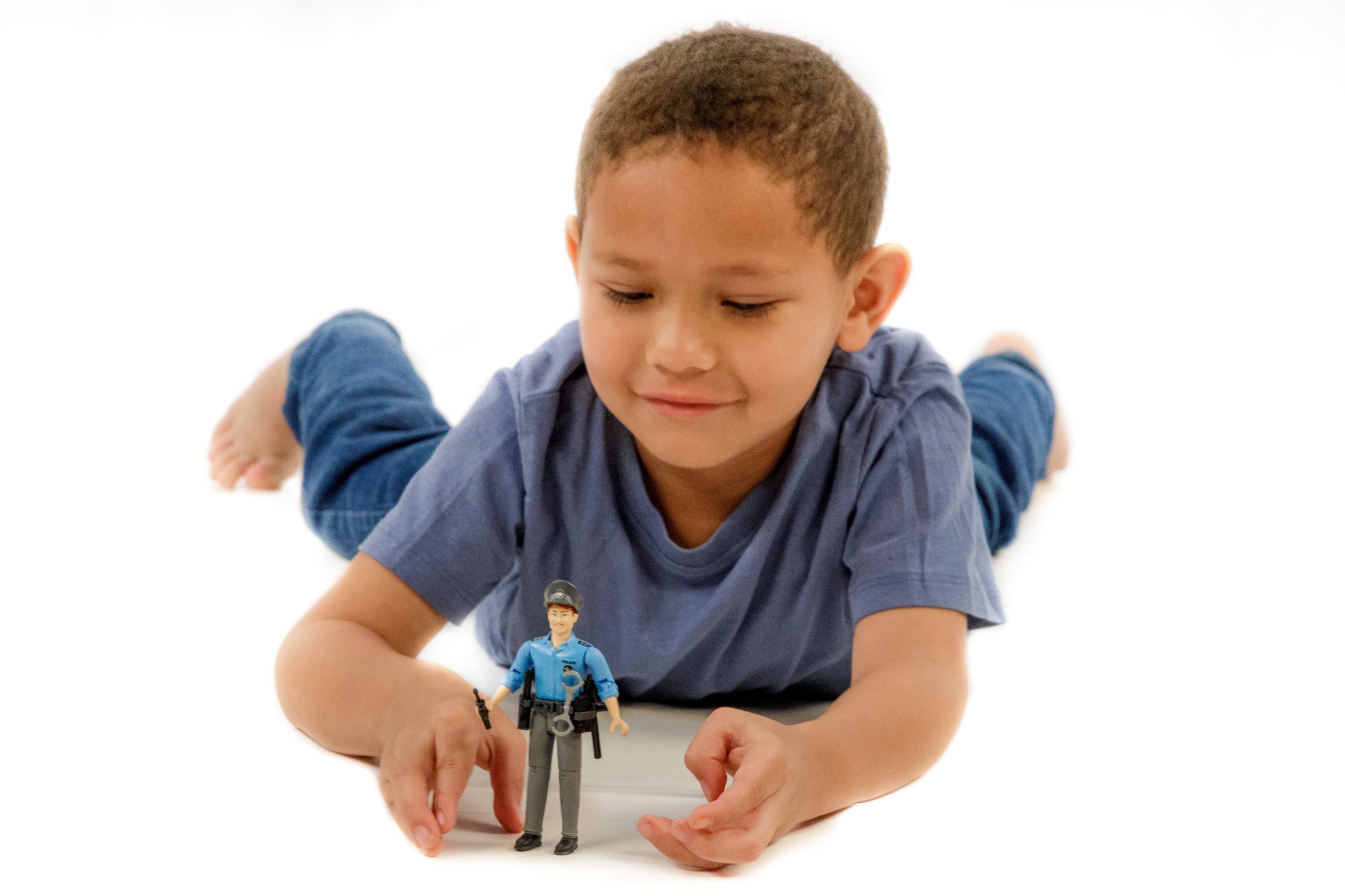 Child lying down playing with Bruder Toys light skin policeman action figure in blue uniform with accessories