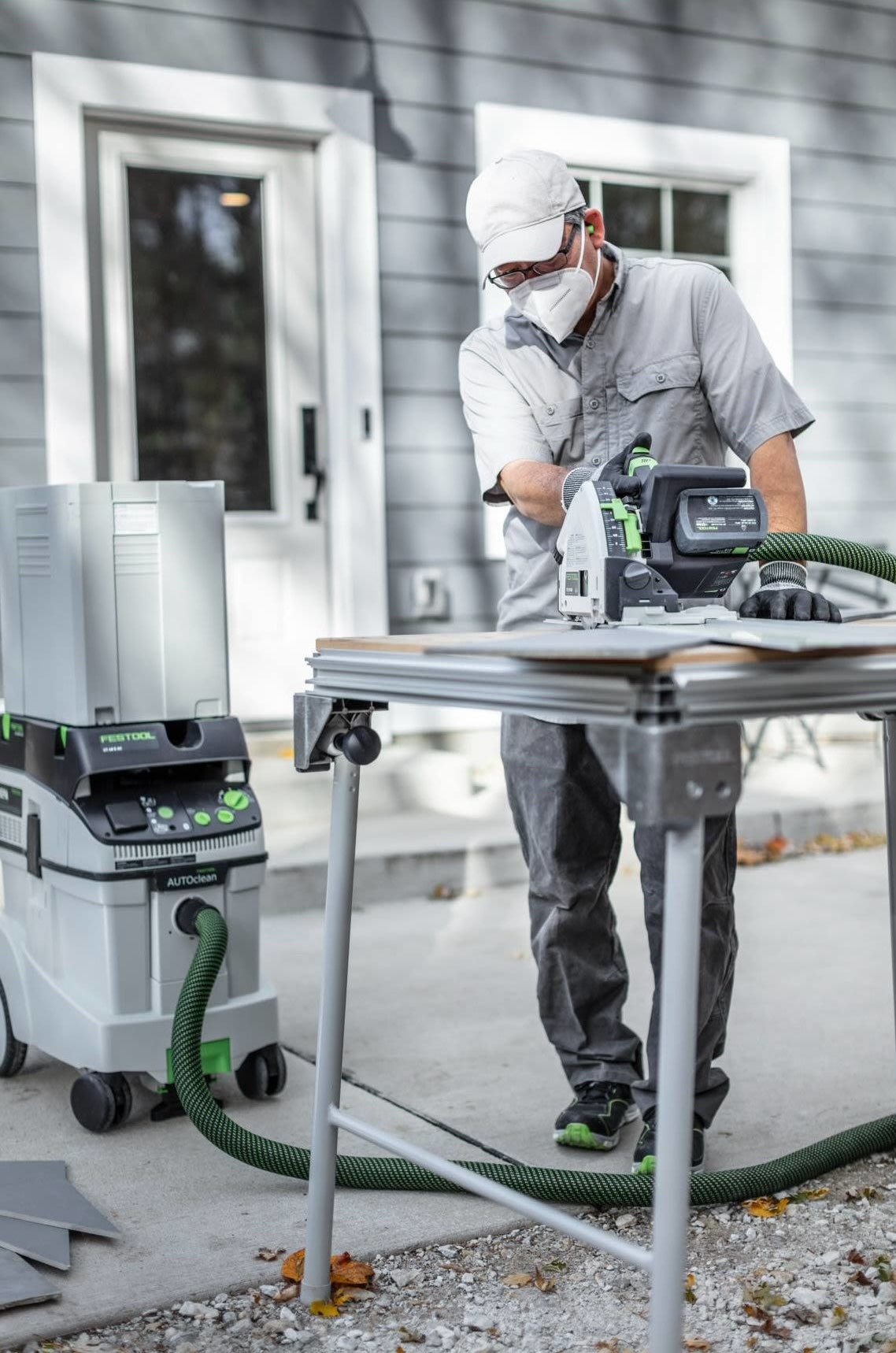 Person wearing protective gear using Festool cordless track saw with dust extractor for outdoor woodworking project