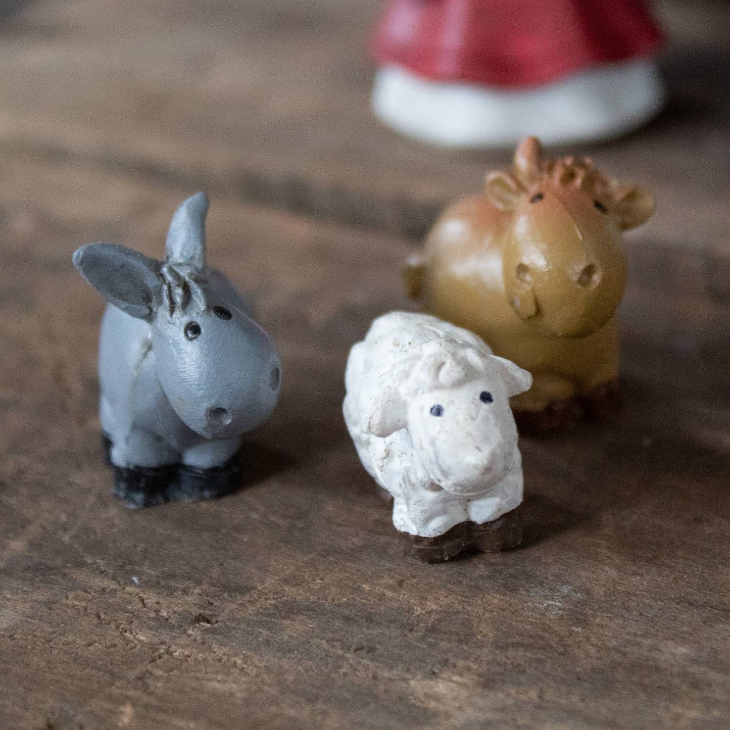 Small hand-painted nativity animal figurines including donkey, sheep, and ox on rustic wood surface for Christmas decor
