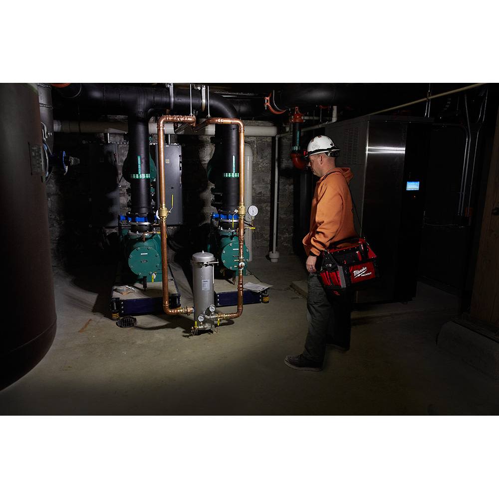 Worker wearing LED headlamp and hard hat inspecting plumbing system in dimly lit utility room for home improvement