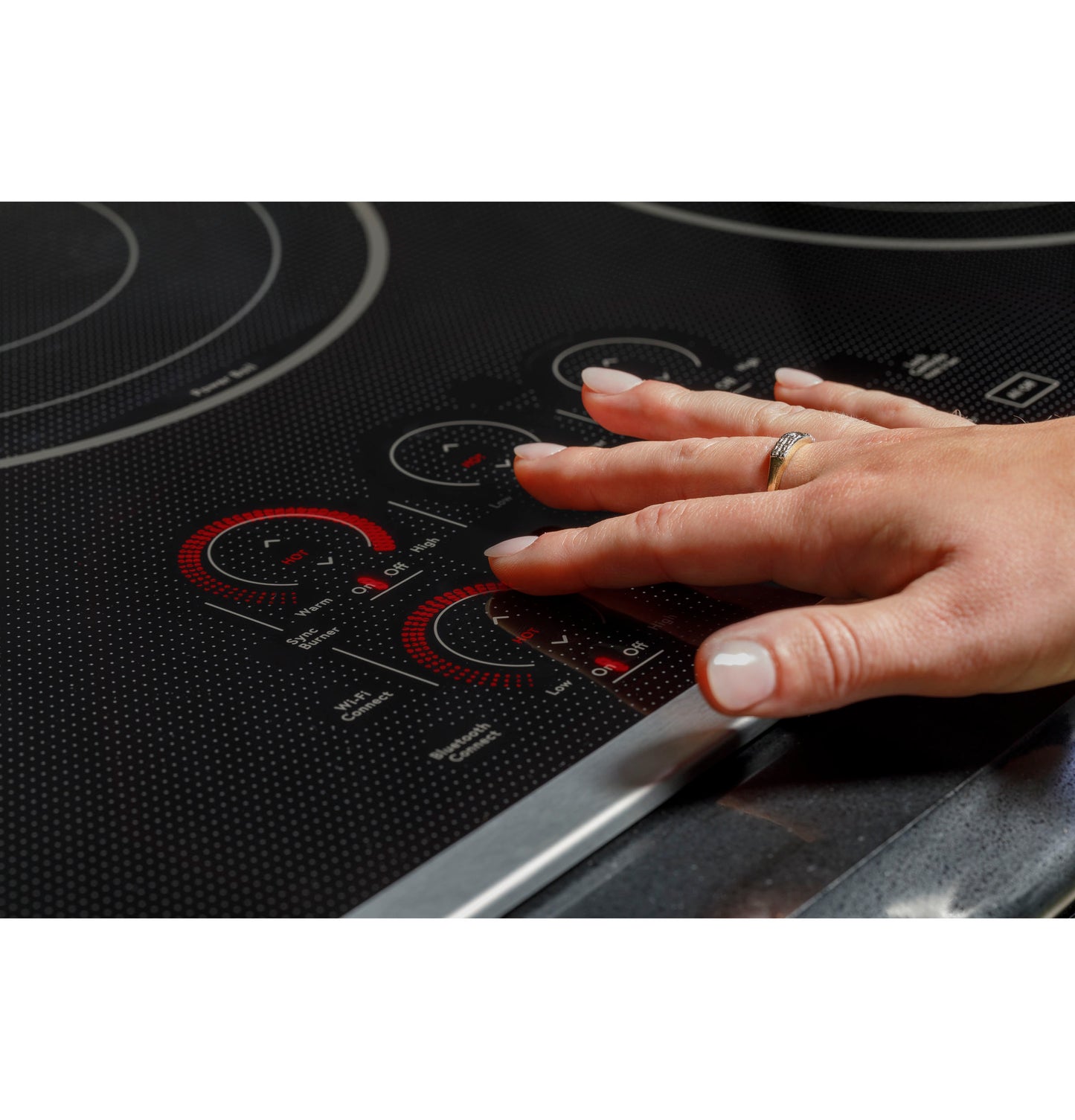 Hand adjusting red digital touch controls on black glass surface of a modern electric cooktop in home kitchen setting