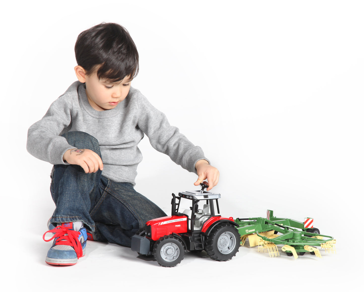 Child playing with red toy tractor and green swath windrower from Vehicles & Remote Controlled Toys collection